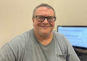 professor wearing a gray shirt sitting in front of a computer